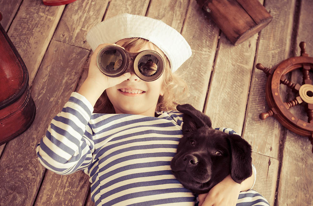 Happy kid dressed in sailor. Child playing with dog at home. Travel and adventure concept